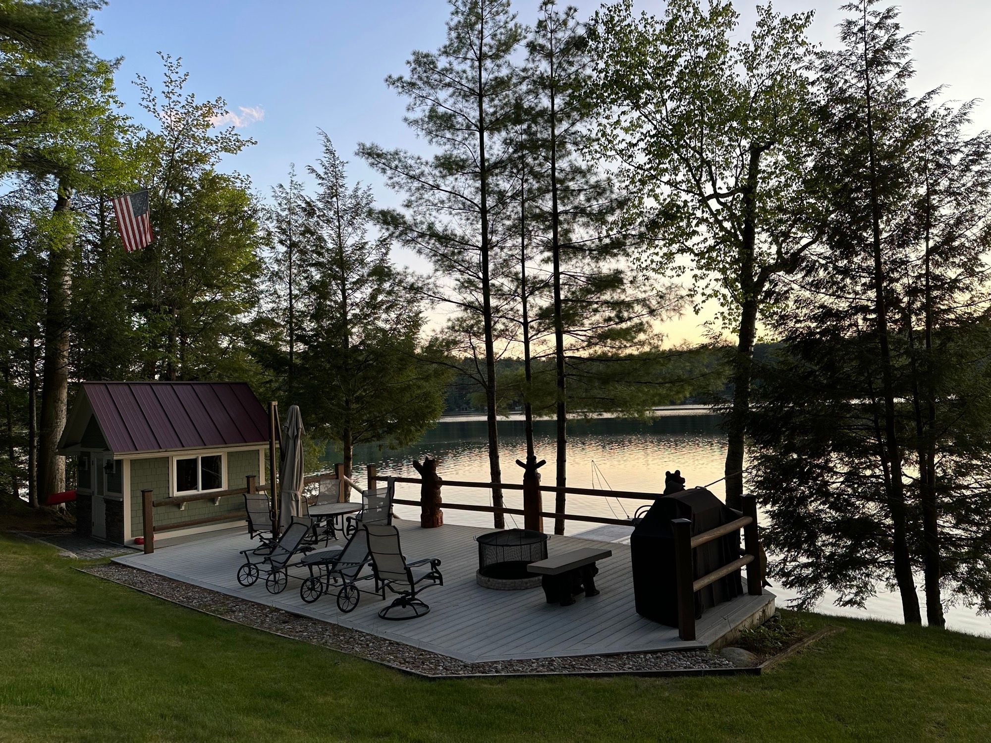 The boathouse deck at Camp Sunnyside at dusk, with loungers, a fire pit, and a grill above Friends Lake.