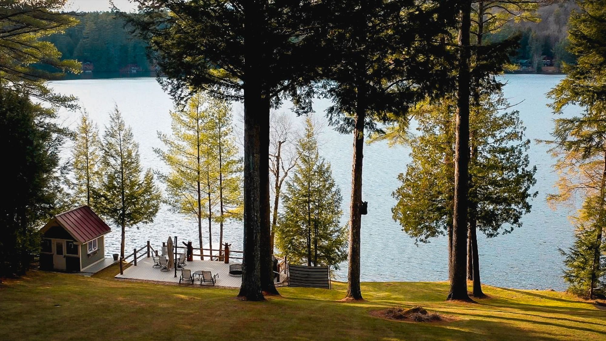 The boathouse and lakeside deck at Camp Sunnyside seen through the pines in golden light.