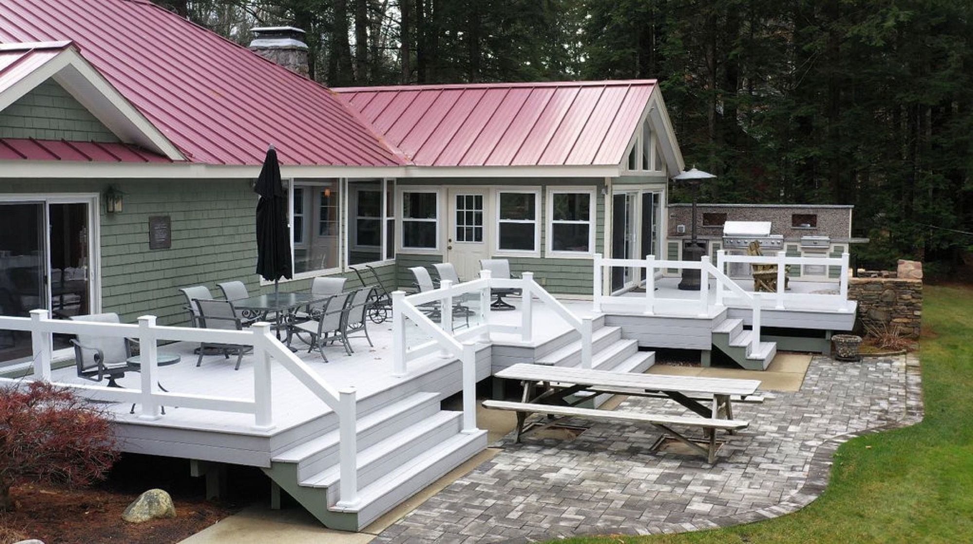 The wraparound deck at Camp Sunnyside with dining tables under the main house's red metal roof.