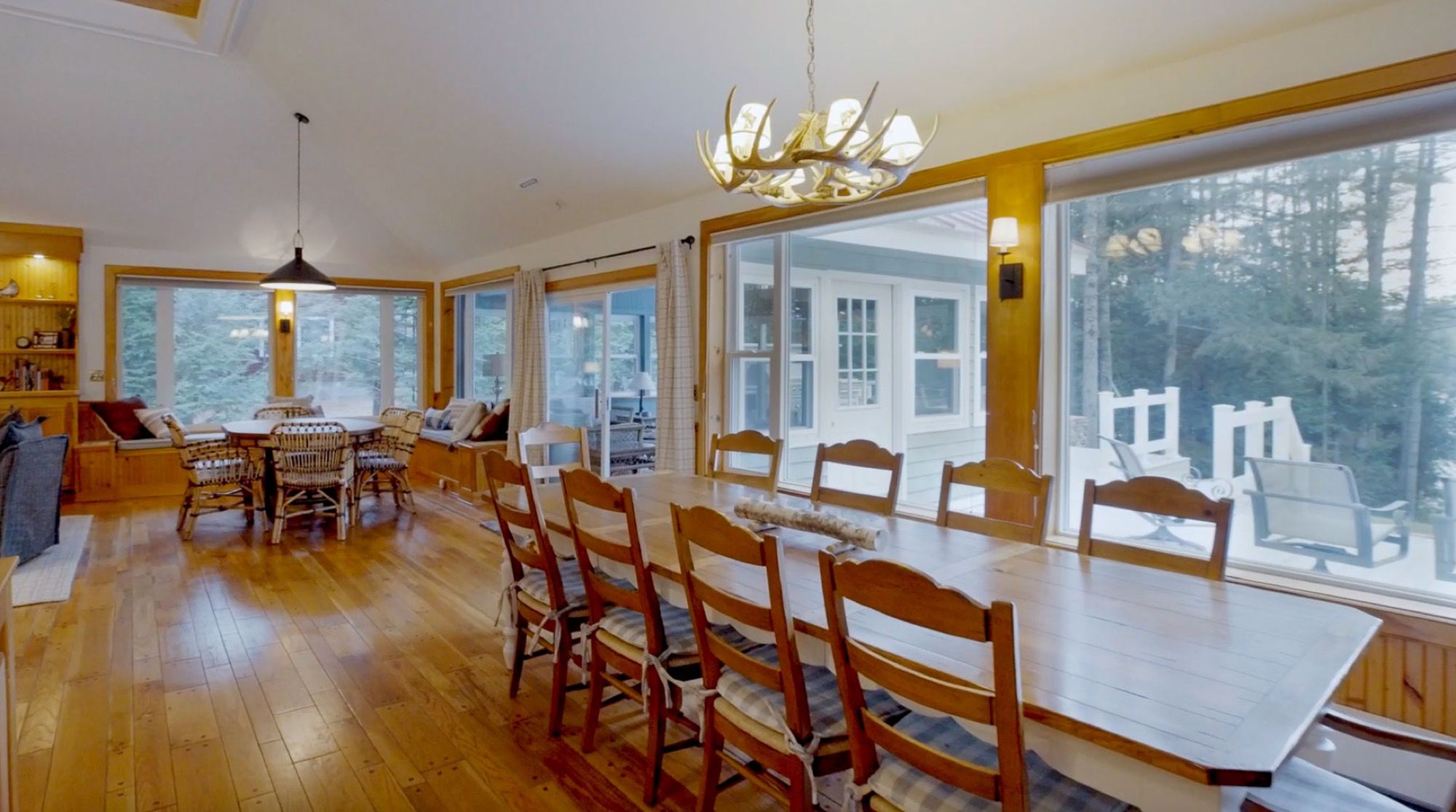 The dining table at Camp Sunnyside set for ten under an antler chandelier, with the lake beyond the windows.