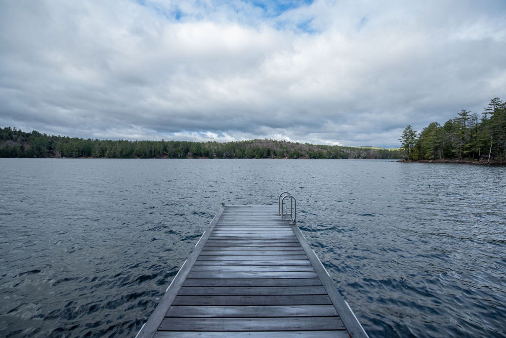 The dock at Camp Sunnyside pointing into Friends Lake under a wide, cloudy sky.