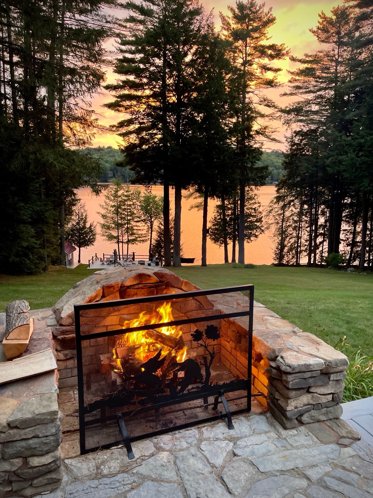 A fire burning in the stone fire pit at Camp Sunnyside as the sun sets over Friends Lake.