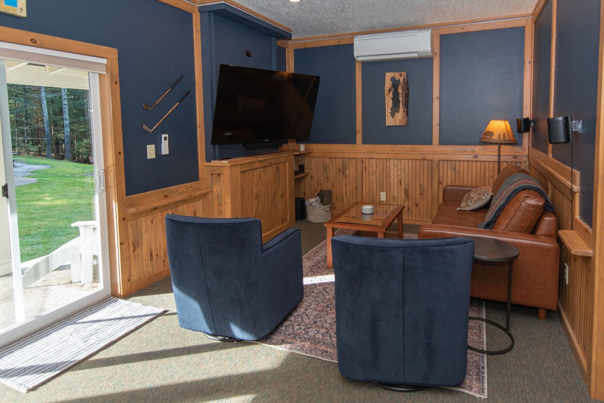 The game house lounge at Camp Sunnyside with a big-screen TV, leather sofa, and sliding doors to the lawn.