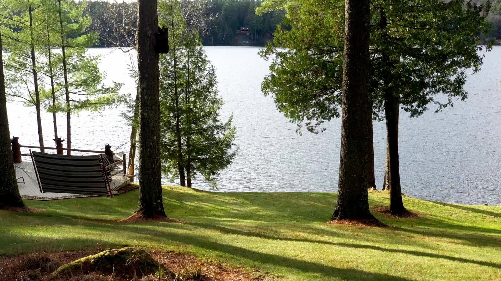 The lakefront lawn at Camp Sunnyside, a private camp on Friends Lake in the Adirondacks, with a hammock under tall pines at the water's edge.