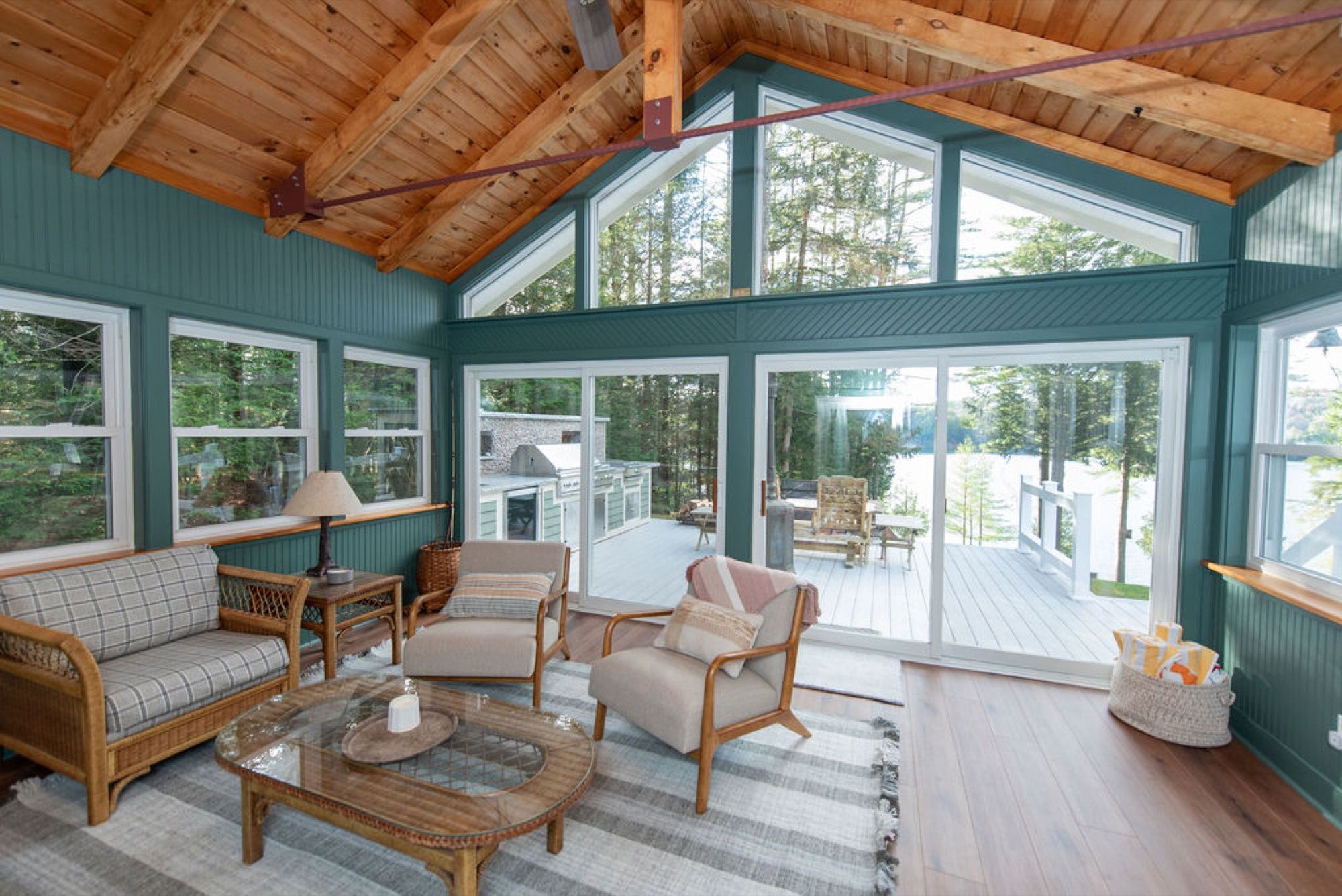 The vaulted sunroom at Camp Sunnyside with green walls, wicker seating, and a wall of windows to the deck and lake.